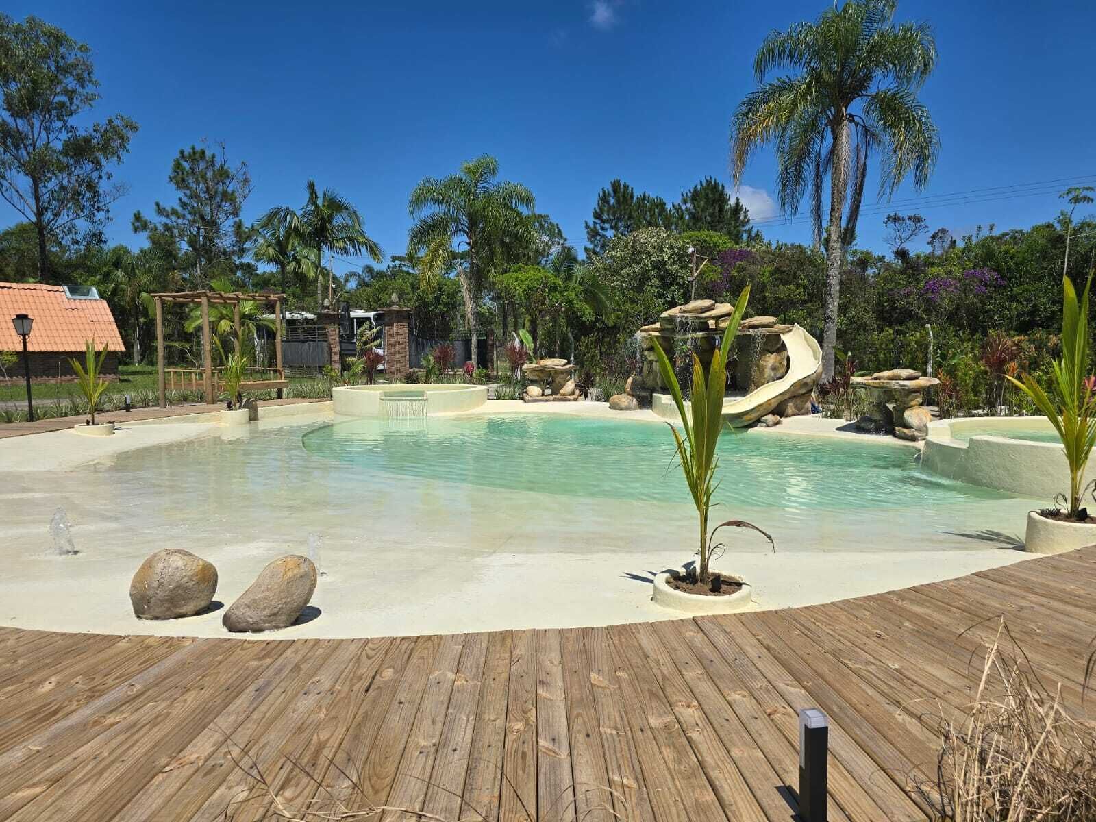 A pool area with a wooden deck, palm trees, and a waterfall feature.