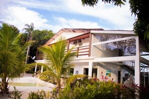 A modern two-story building with a glass facade, surrounded by lush greenery and a small pool.