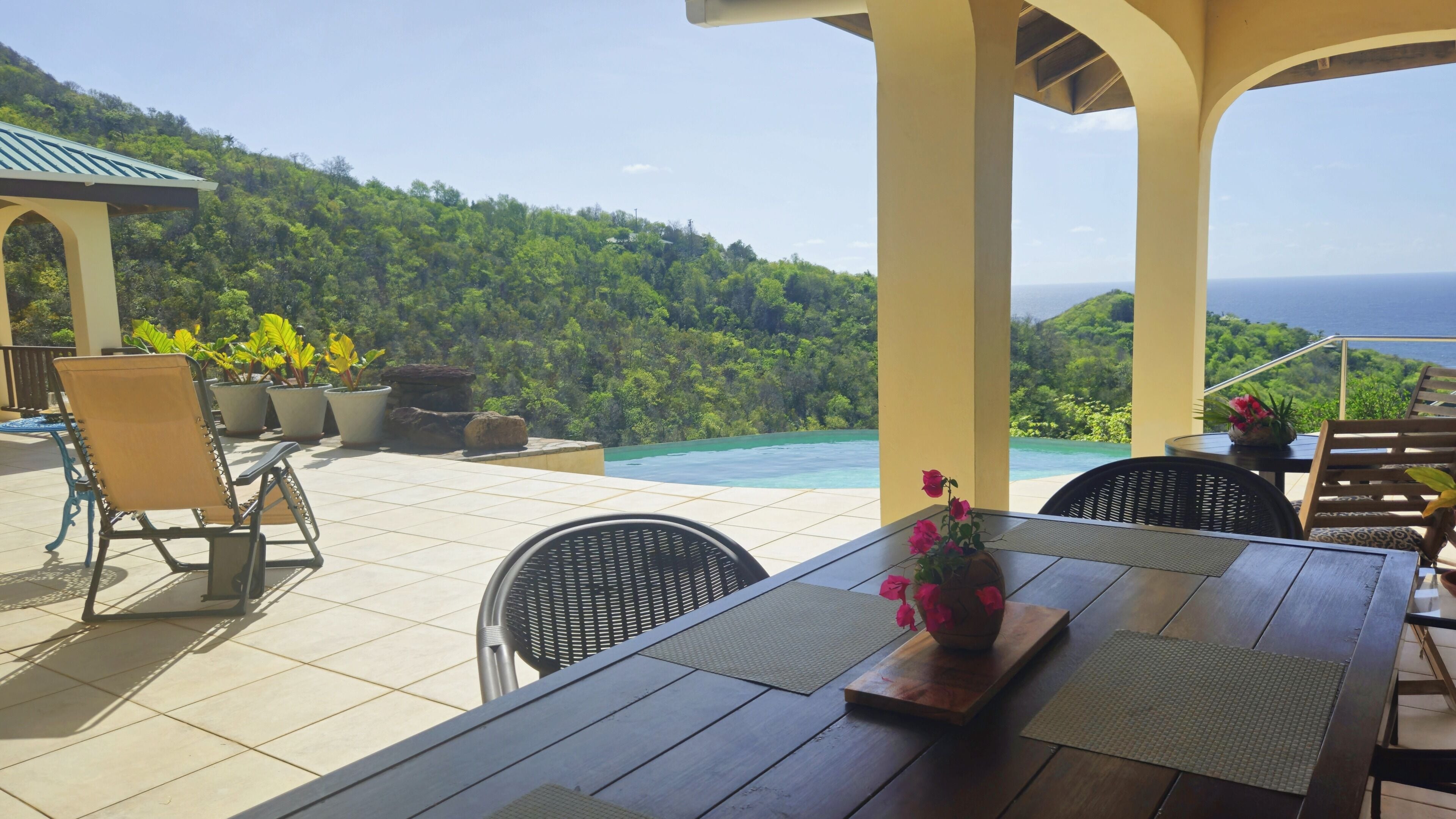 An outdoor patio with a pool, chairs, and a table with a vase of flowers.