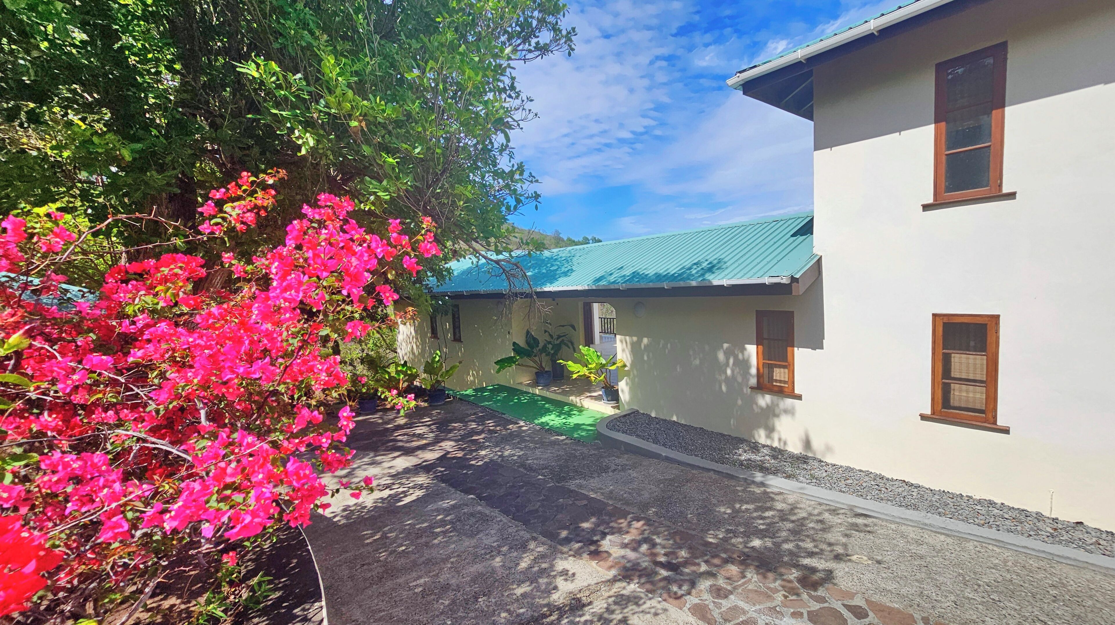 A building with a green roof, a paved pathway, and a garden with pink flowers.