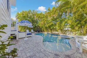 Ein Pool mit gewölbter Kante, umgeben von einer gepflasterten Terrasse und weißen Liegestühlen.