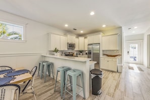A modern kitchen with white cabinetry, a central island, bar stools, and a trash can. - Sunnyside of the Beach: Updated, 5-bedroom home, pool, close to beach! (Holmes Beach)