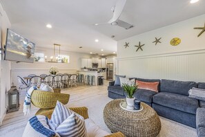 A modern living room with a grey sofa, wicker furniture, and a flat-screen TV mounted on the wall. - Sunnyside of the Beach: Updated, 5-bedroom home, pool, close to beach! (Holmes Beach)