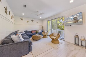 A spacious living room with a grey sectional sofa, wicker chairs, and a large window offering a view of the outdoors. - Sunnyside of the Beach: Updated, 5-bedroom home, pool, close to beach! (Holmes Beach)