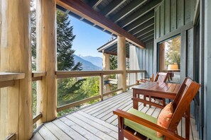 A wooden deck with a table and chairs, overlooking a mountainous landscape. - Mountain view townhome w/ ski access & hot tub (Whistler)