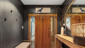 Uma casa de banho moderna com um banco, porta de madeira e um espelho com decoração de pássaro.
