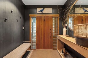 A modern bathroom with a bench, wooden door, and a mirror with a bird decoration. - Mountain view townhome w/ pool & hot tub (Whistler)