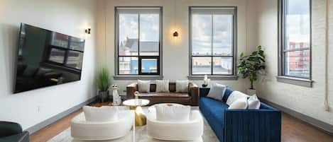 A spacious living room with a large flat-screen TV, two sofas, a coffee table, and a potted plant.