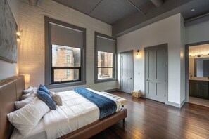 A spacious bedroom with a large bed, a wooden floor, and a view of the outside through a window. - Luxury 6BR Retreat w Rooftop Deck at TQL Stadium (Cincinnati)