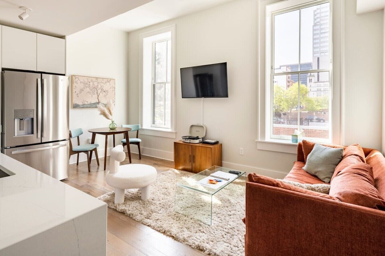 A modern apartment with a kitchen, dining area, living room, and a large window with a city view.