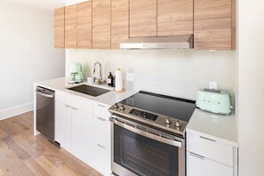A compact kitchen with a dishwasher, a stovetop with an oven, a toaster, and wooden cabinets. - Centrally Located, Free Garage Parking! (Cincinnati)