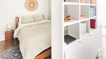 A bedroom with a bed, a bedside table, a wall hanging, and a bookshelf.