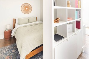 A bedroom with a bed, a bedside table, a wall hanging, and a bookshelf. - Centrally Located, Free Garage Parking! (Cincinnati)
