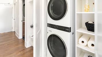 A laundry room with two front-loading washing machines, a shelf with rolls of toilet paper, and a basket on the shelf.