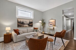 A modern living room with a sofa, coffee table, and chairs, a painting on the wall, and a window. - Lux Historic 2BR near Stadiums, Downtown (Cincinnati)