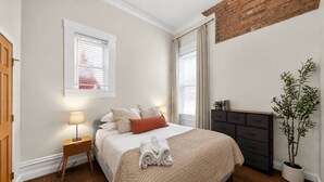 A bedroom with a bed, bedside lamps, a dresser, and a potted plant. - Lux Historic 2BR near Stadiums, Downtown (Cincinnati)