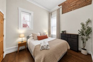 A bedroom with a bed, bedside lamps, a dresser, and a potted plant. - Lux Historic 2BR near Stadiums, Downtown (Cincinnati)