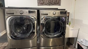 A laundry area with two stainless steel front-loading washers and dryers, a 'Laundry' sign on the wall, and a small sink with a trash can.