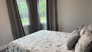 A bedroom with a bed, grey curtains, and a window.