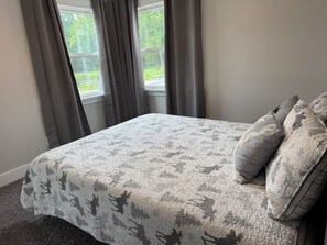Un dormitorio con cama, cortinas grises y una ventana.