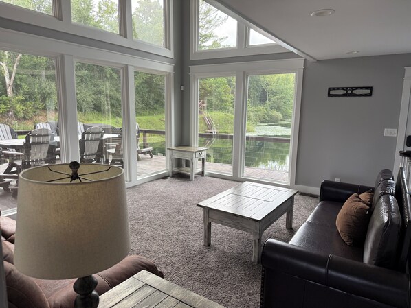 A room with large windows, a sofa, a table, and a lamp.