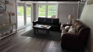 A living room with a black leather sofa, a wooden coffee table, and a brown leather couch. There is a large window with a view of greenery outside.