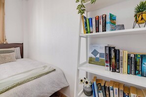 A bedroom with a neatly made bed, a white bookshelf filled with books, and a small potted plant on the shelf. - CB Living - Homely apartment Ciñuelica, Punta Prim (Alicante / Alacant)