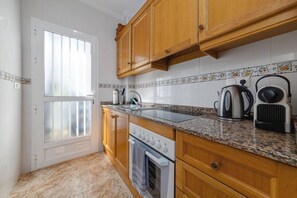 A kitchen with wooden cabinets, a granite countertop, a stove, and a kettle. - CB Living - Homely apartment Ciñuelica, Punta Prim (Alicante / Alacant)