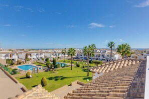 A residential area with a swimming pool, palm trees, and a view of the sea. - CB Living - Homely apartment Ciñuelica, Punta Prim (Alicante / Alacant)