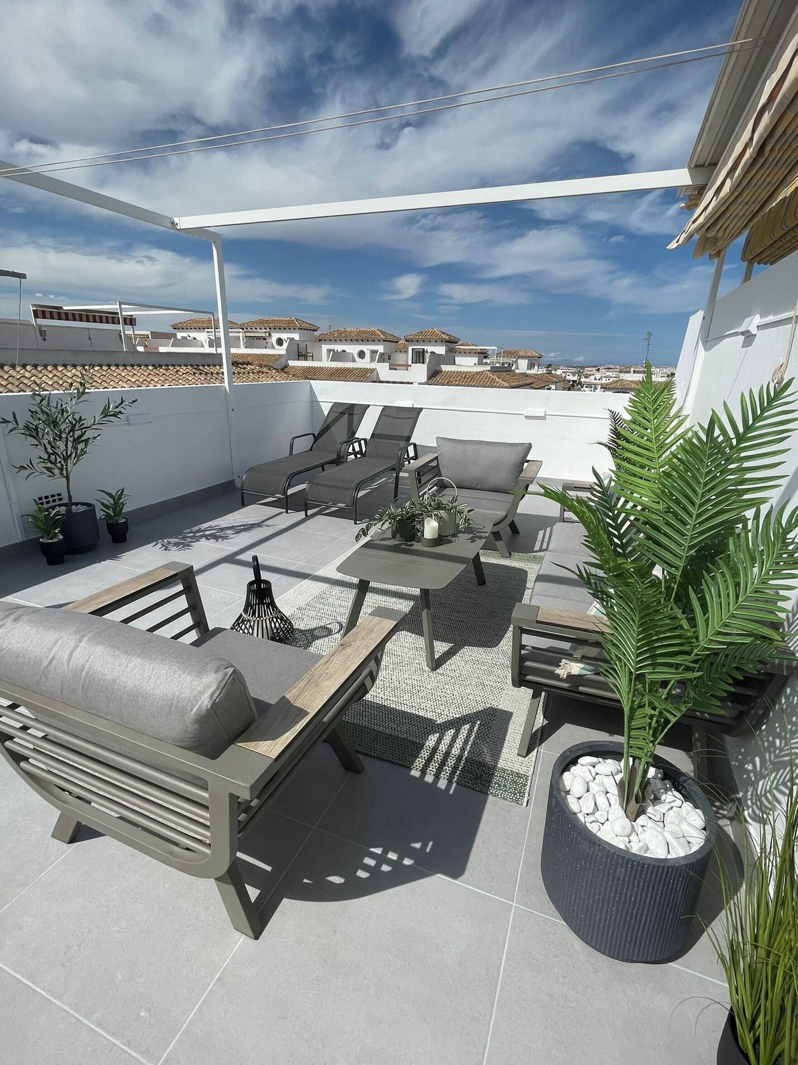 Terraza en la azotea con mobiliario exterior, plantas en macetas y vistas a edificios distantes.