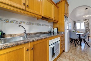 Una cocina con gabinetes de madera, encimera de granito, pileta de acero inoxidable y horno empotrado.