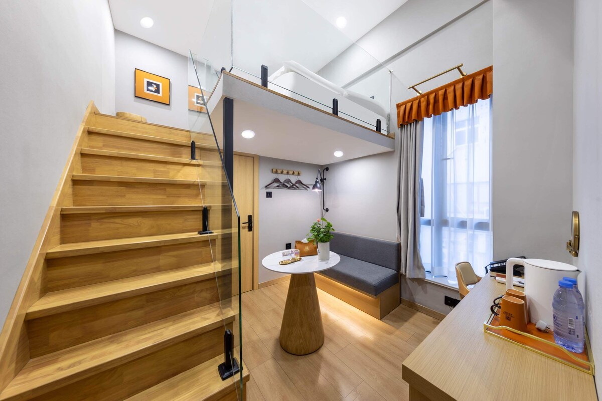 Un interior moderno con una escalera de madera, una mesa redonda con una planta, un sofá y un comedor con mesa y sillas.