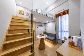 Un interior moderno con una escalera de madera, una mesa redonda con una planta, un sofá y un comedor con mesa y sillas.