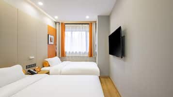 Habitación de hotel con dos camas, televisión, ventana con cortinas y mesita de noche con lámpara y teléfono.