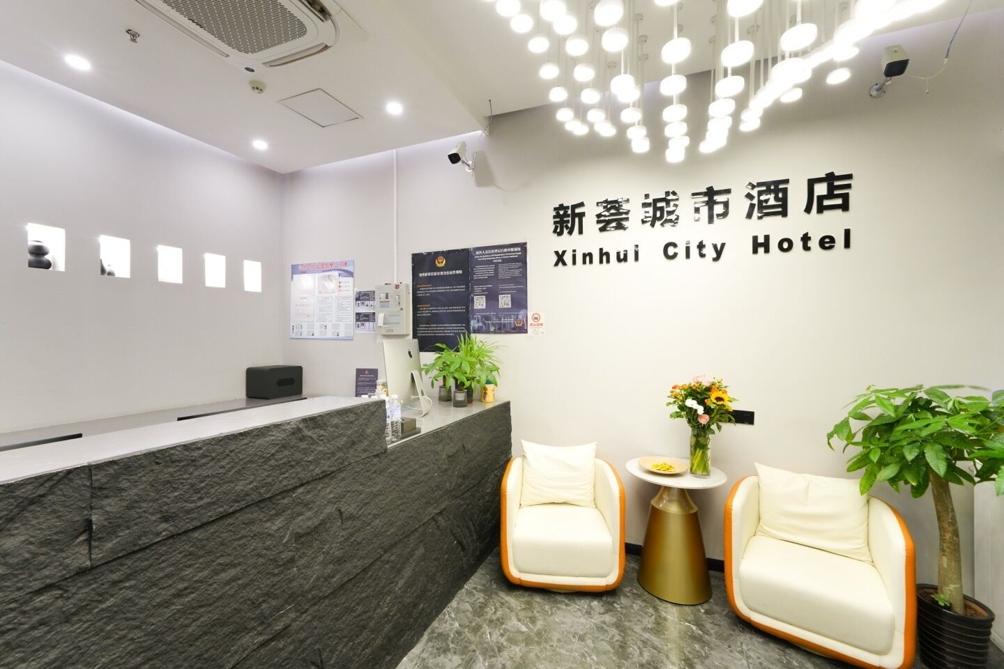 Zona de recepción de hotel con mostrador de mármol, dos sillones, una pequeña mesa con un jarrón de flores y una pared con el nombre del hotel en chino e inglés.