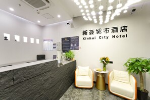 Uma área de recepção de hotel com balcão de mármore, duas poltronas, uma mesa pequena com um vaso de flores e uma parede com o nome do hotel em chinês e inglês.