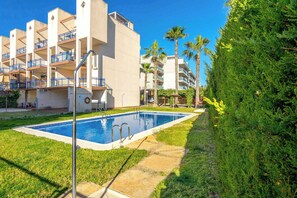 A swimming pool with a clear blue water surface, surrounded by a well-maintained lawn and a hedge. - CB Living - Apartment with roof terrace Aguamarina (Orihuela)