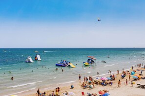 A beach with people, inflatable water structures, and boats. - CB Living - Apartment with roof terrace Aguamarina (Orihuela)