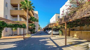 Una strada fiancheggiata da edifici, auto parcheggiate e palme.
