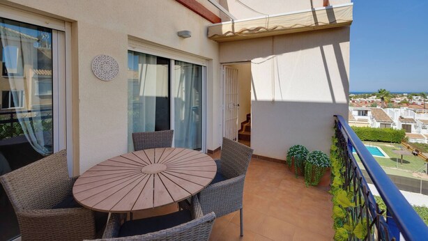 Un balcone con un tavolo rotondo e sedie in vimini, vista sul mare e area piscina sullo sfondo.