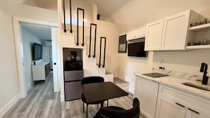 Een moderne keuken met witte kastjes, een zwart aanrechtblad en een eethoek met tafel en stoelen.