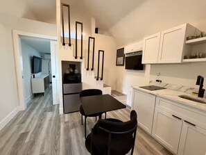 A modern kitchen with white cabinetry, a black countertop, and a dining area with a table and chairs. - Safari Tiny House Escape Nice, quiet, and private (Tampa)