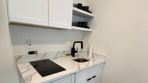 Een kleine keuken met witte kastjes, een marmeren aanrechtblad, een zwarte kraan en een zwart tabletje op het aanrecht.