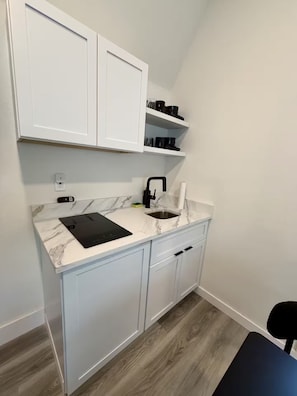 A compact kitchen with white cabinets, a marble countertop, a black faucet, and a black tablet on the counter. - Safari Tiny House Escape Nice, quiet, and private (Tampa)