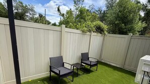 Een achtertuin met kunstgras, twee zwarte stoelen en een witte schutting.