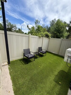 A backyard with artificial grass, two black chairs, and a white fence. - Safari Tiny House Escape Nice, quiet, and private (Tampa)