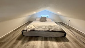 Een kamer met een schuine kap, een bed, een raam en een stopcontact.