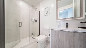 A modern bathroom with a glass-enclosed shower, a toilet, and a vanity with a mirror.