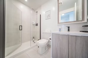 A modern bathroom with a glass-enclosed shower, a toilet, and a vanity with a mirror.