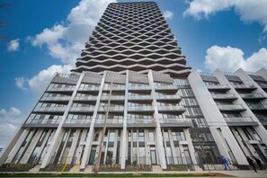 A modern high-rise building with a distinctive geometric facade, multiple balconies, and a clear sky in the background.